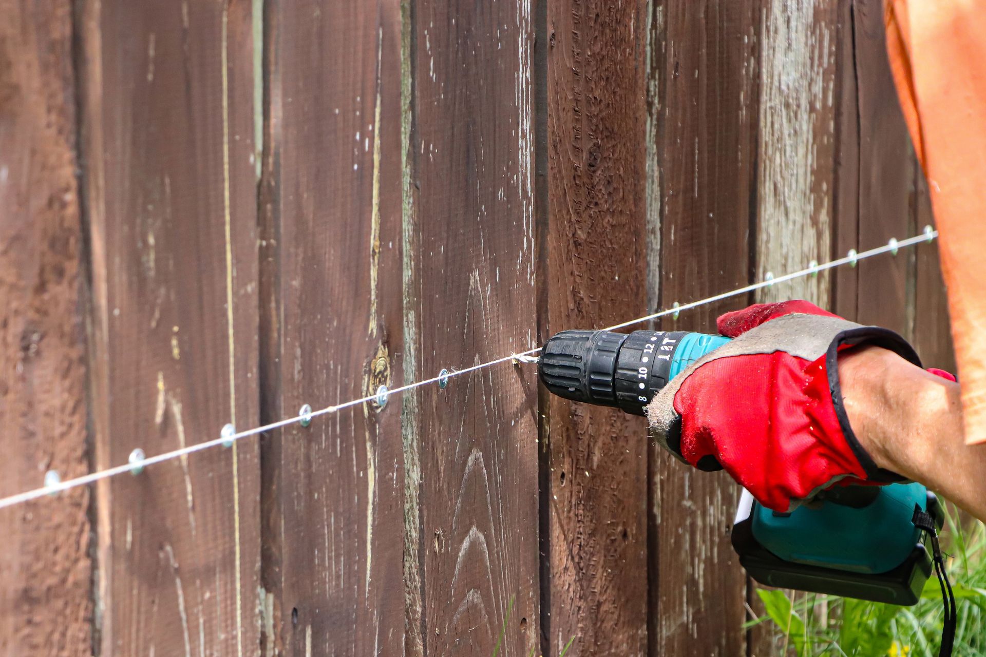 Carpenter’s hands as he uses an electric screwdriver to strengthen a wooden fence.