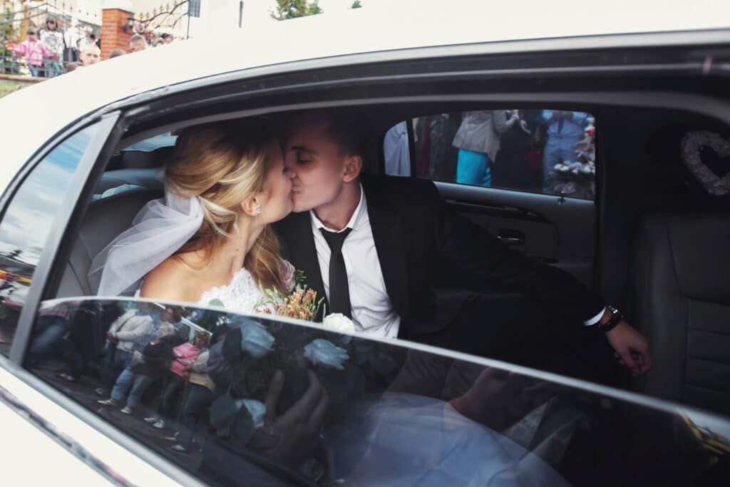 Bride and groom kissing in the back of a white limousine after their wedding.