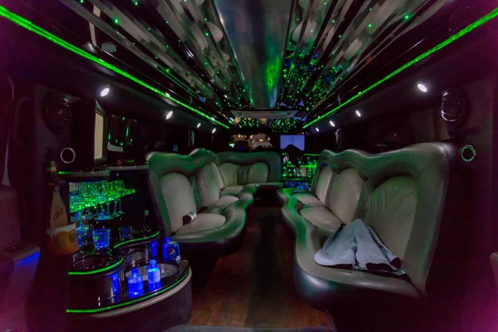Interior of a limousine with green and white lights, seating, and a bar area.
