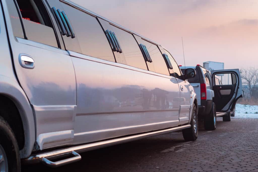 White limousine parked, passenger door open, setting sun in background.