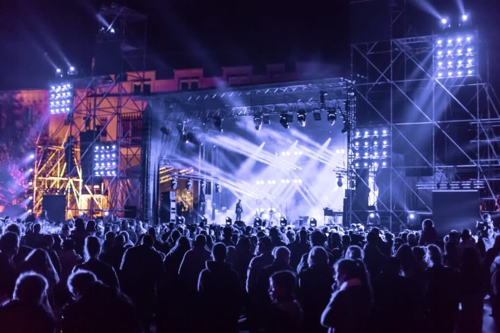 Concert stage with bright blue lights, silhouetted crowd.
