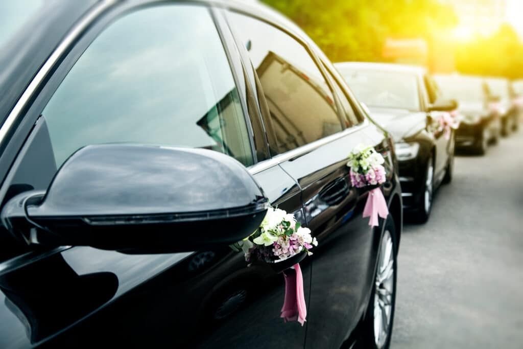 Black cars in a row, decorated with flowers, likely a wedding procession on a sunny day.