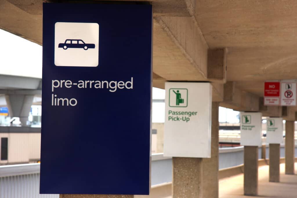 Blue sign: Pre-arranged limo pickup at an airport. White limo icon, white text. Beige columns, walkway.