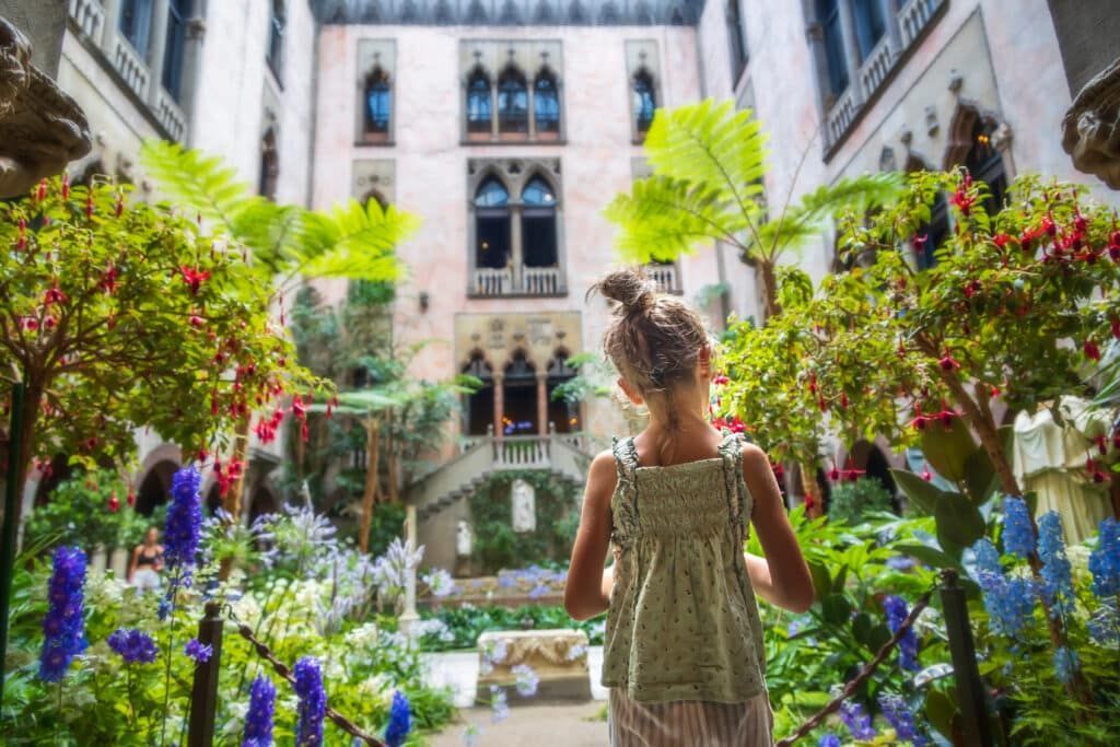 Girl looking at a garden courtyard with colorful flowers and a historic building.