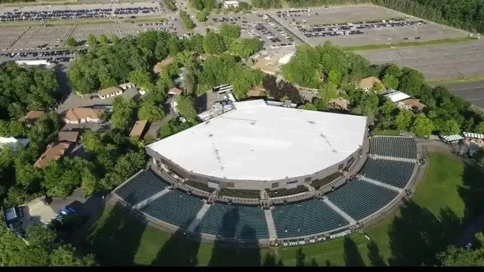 Aerial view of the Saratoga Performing Arts Center outdoor amphitheater with rows of seats and large white roof.