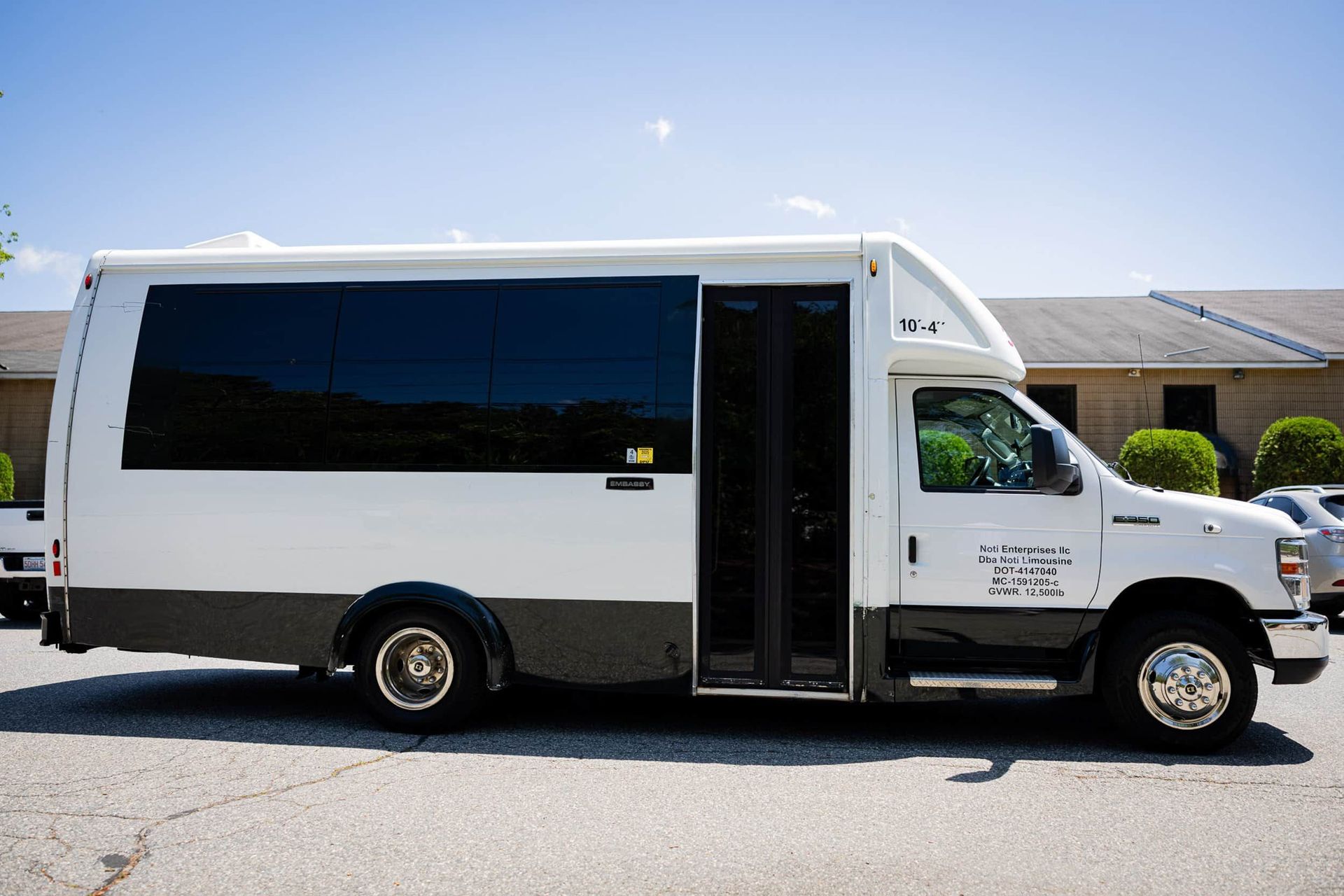 White and dark gray shuttle bus parked outdoors on a sunny day.