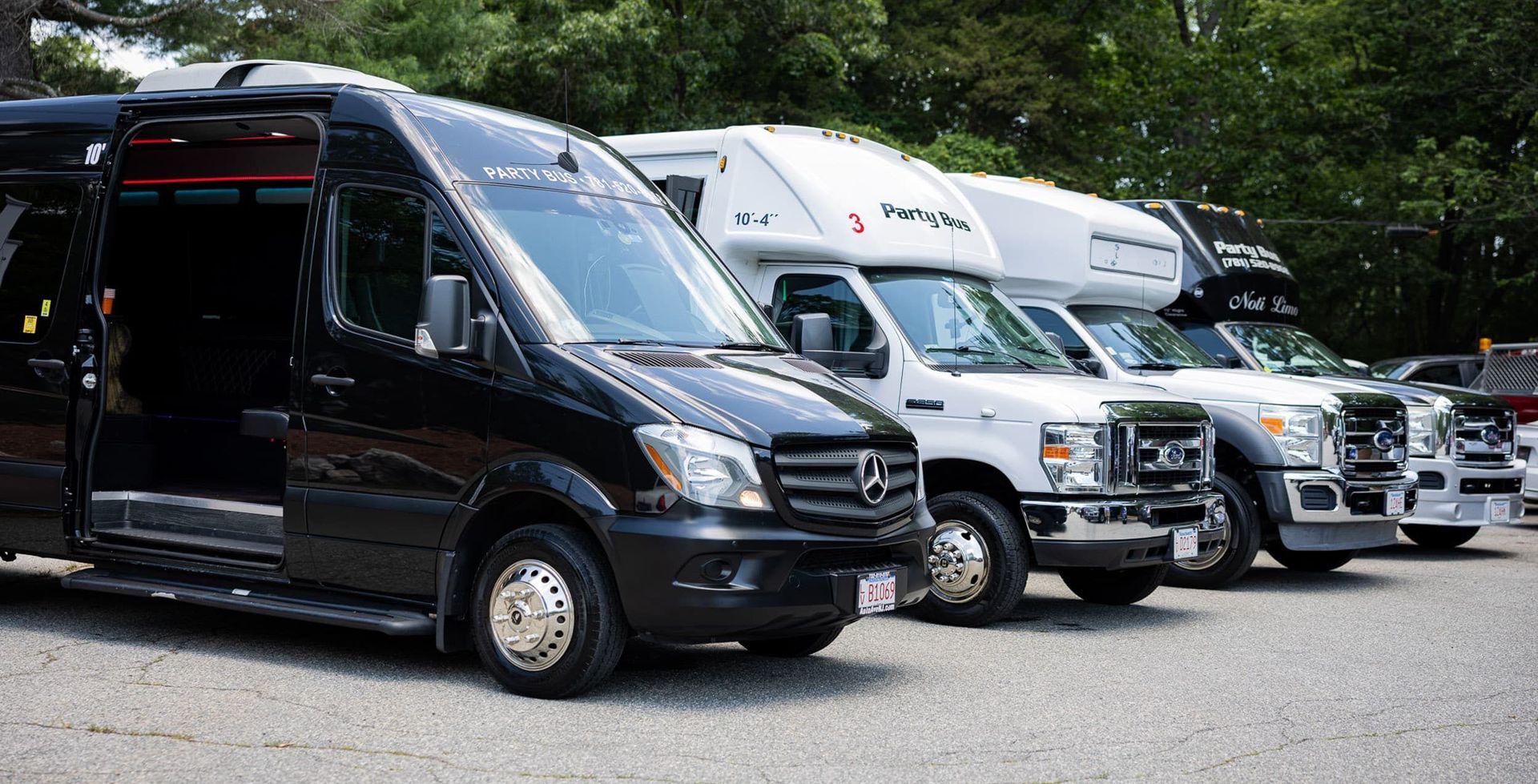 Row of black and white vans parked on pavement, with trees in the background.