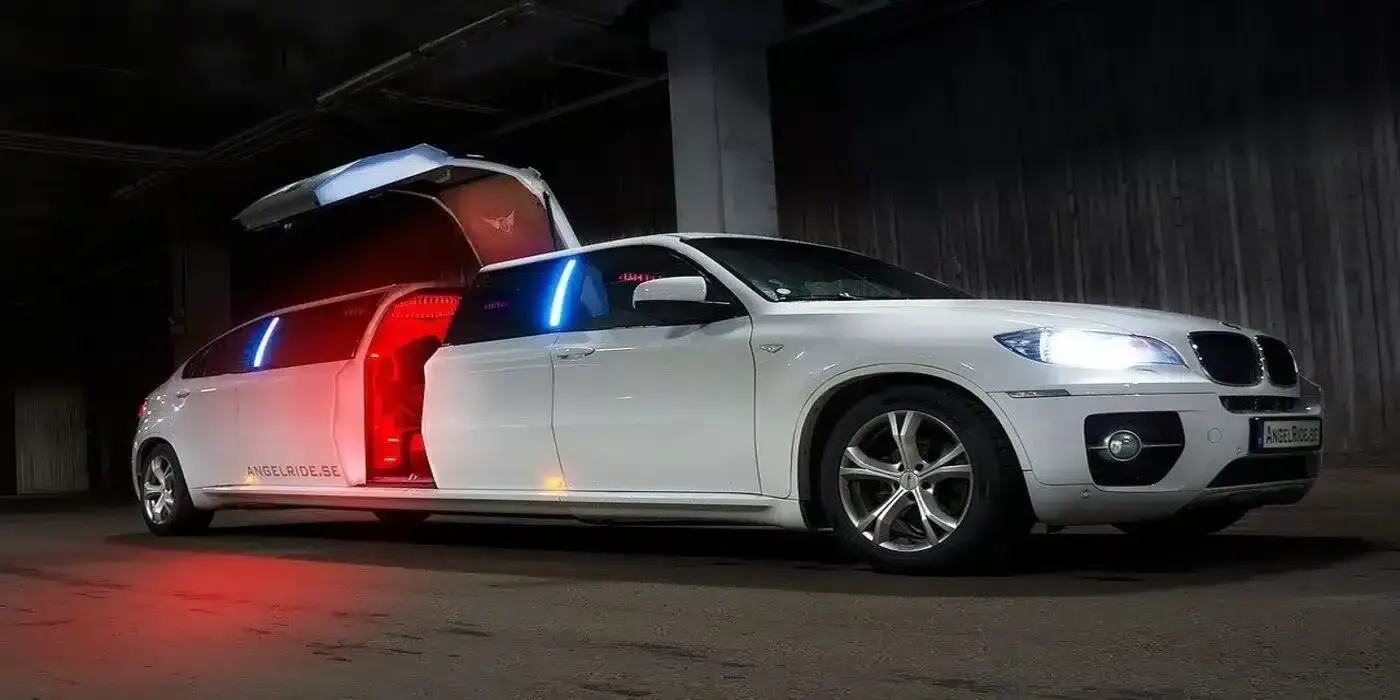 White limousine with gull-wing doors open, lit by red and blue lights. Dark setting.