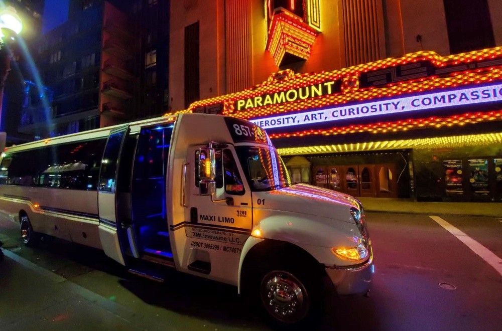A white shuttle bus parked in front of the Paramount Theatre at night.