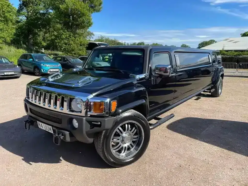 Black Hummer H3 limousine parked on gravel with other cars on a sunny day.