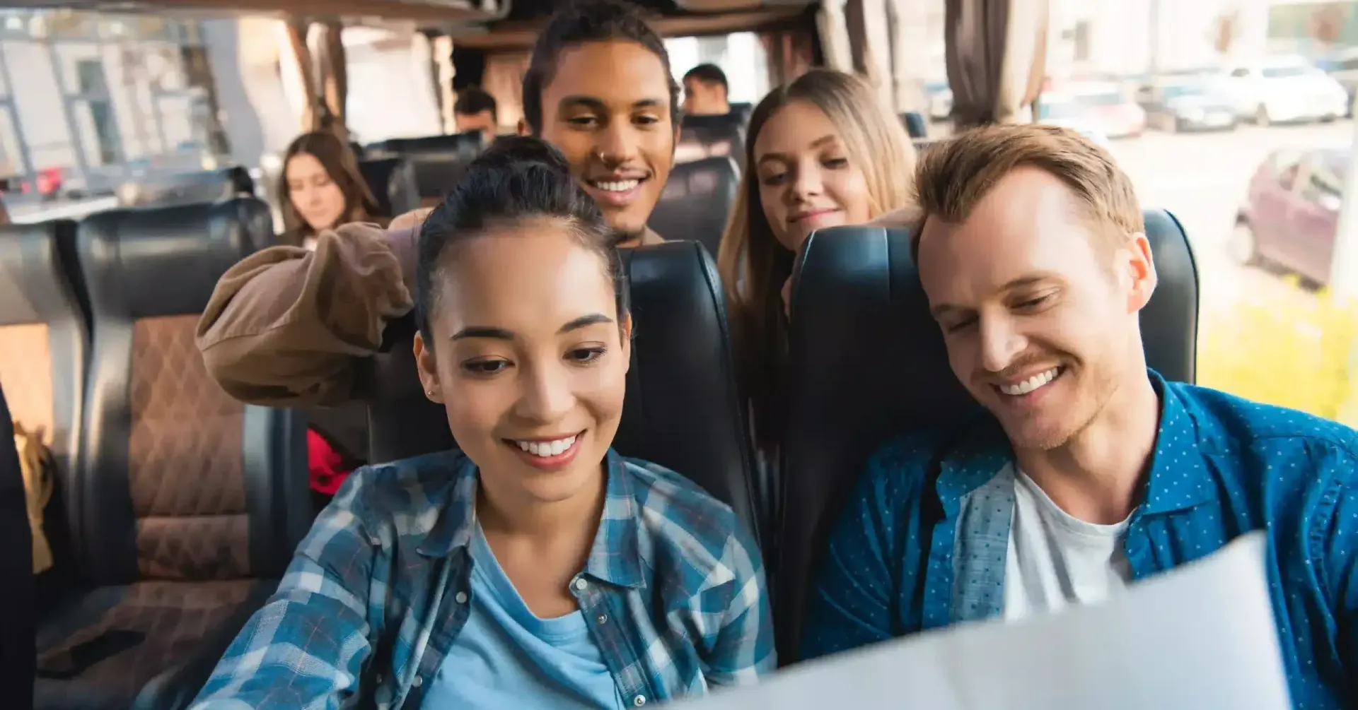 Group of friends smiling and looking at a map on a bus, planning their trip.