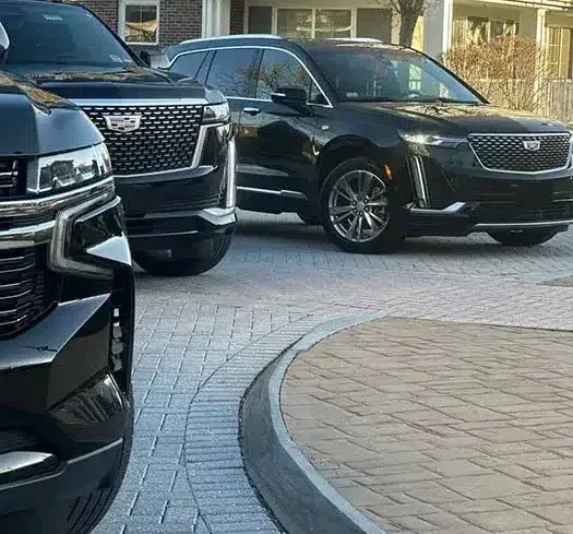 Three black Cadillac SUVs parked on a brick driveway.