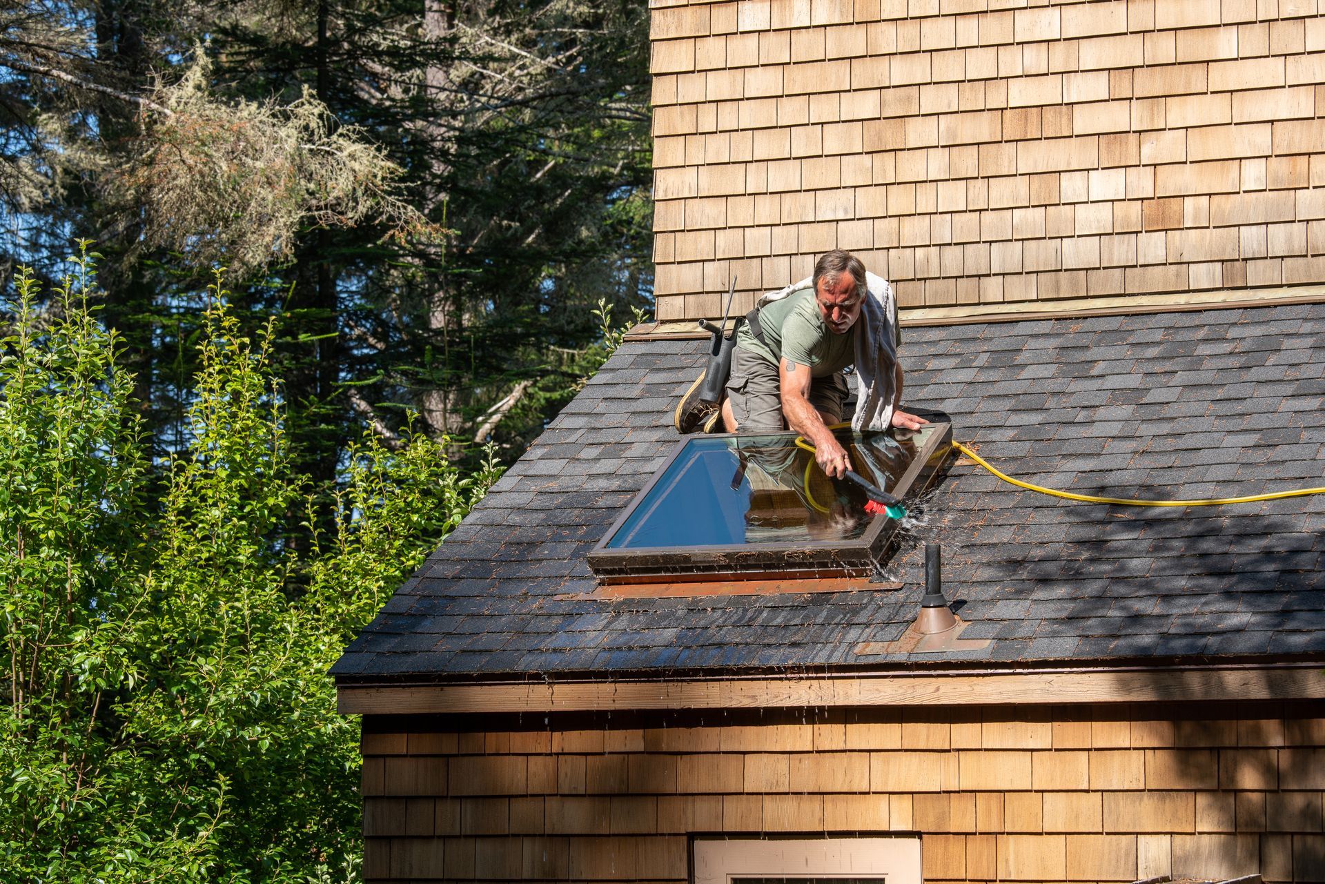 Man washing skylight on roof of house.