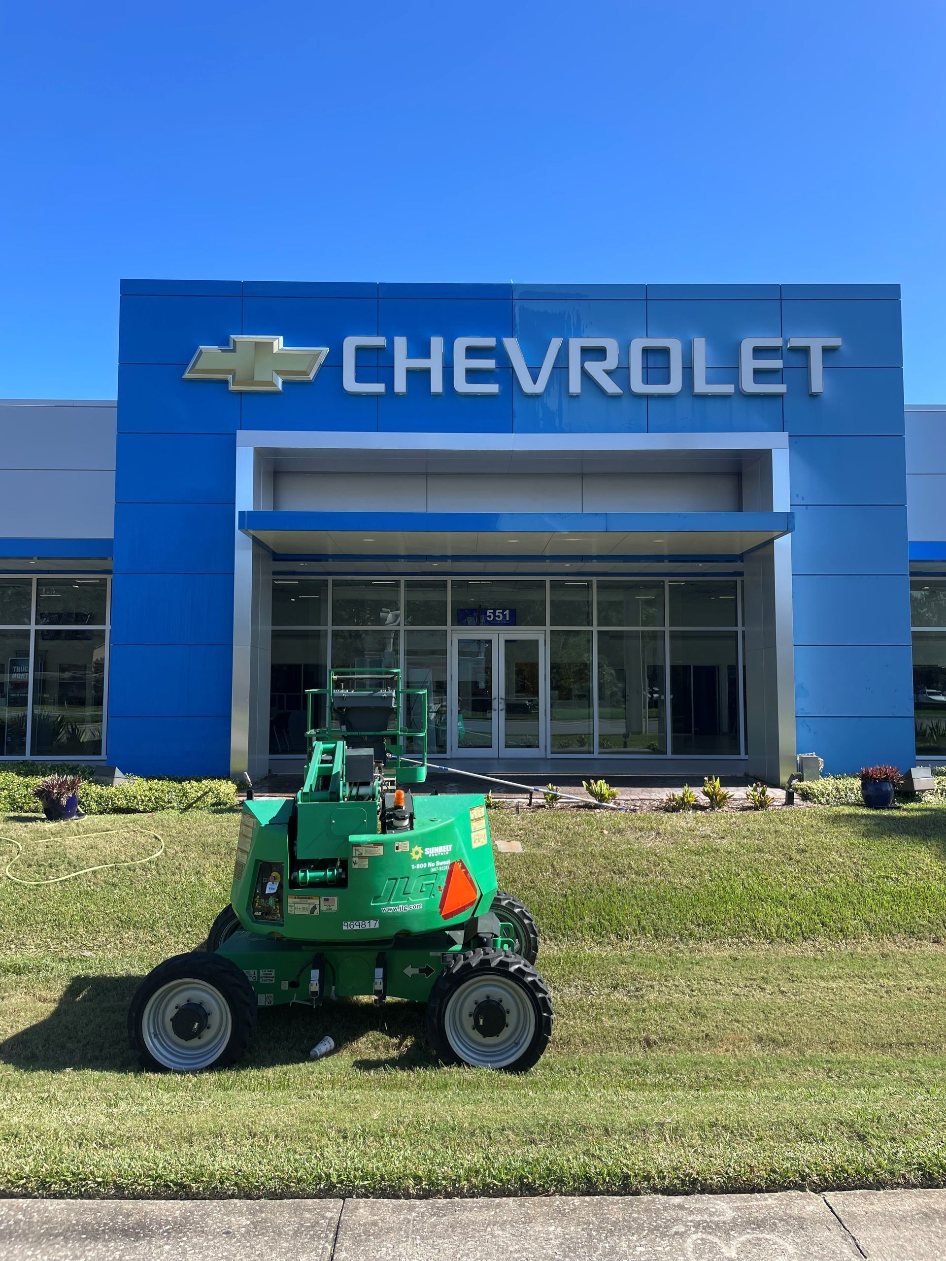 Green lift in front of a blue Chevrolet dealership on a sunny day.