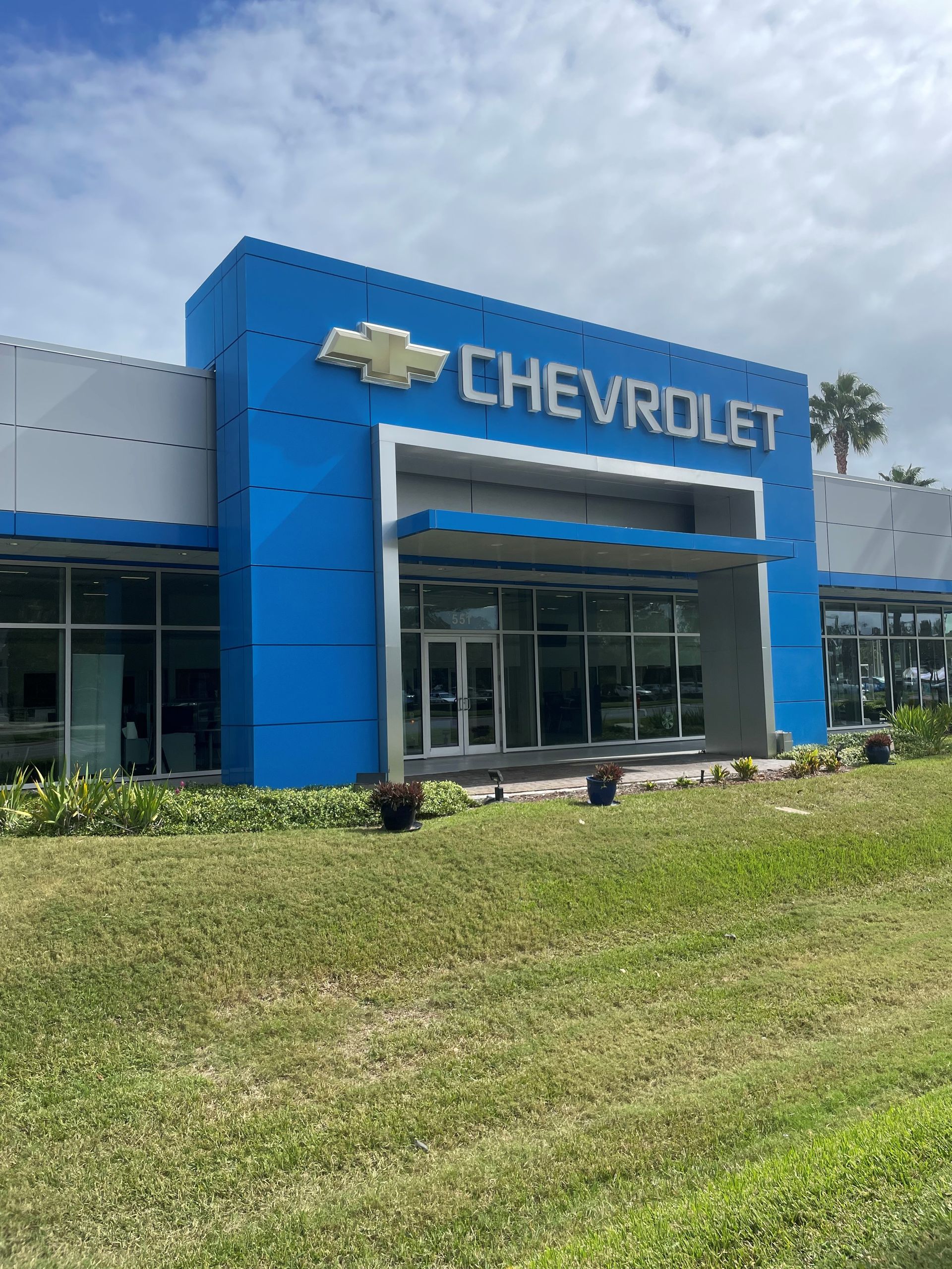 Blue Chevrolet dealership with sign and logo, grass and cloudy sky.