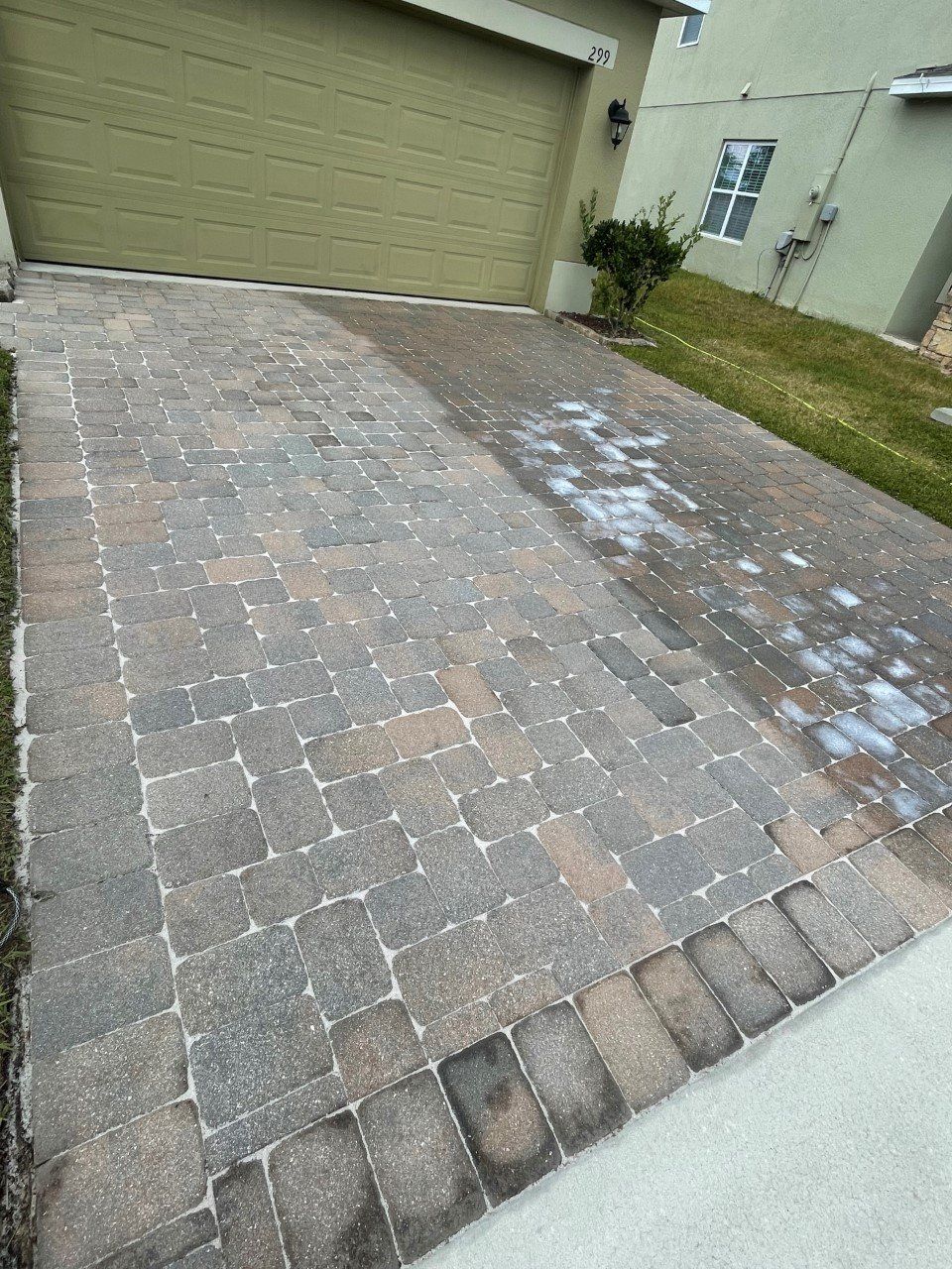 Driveway with brick pavers, partially cleaned with soap, beside a green lawn and garage.