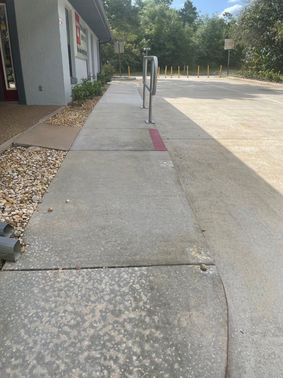 Sidewalk next to a building, featuring a bike rack and a gravel border, with parking lot on the right.