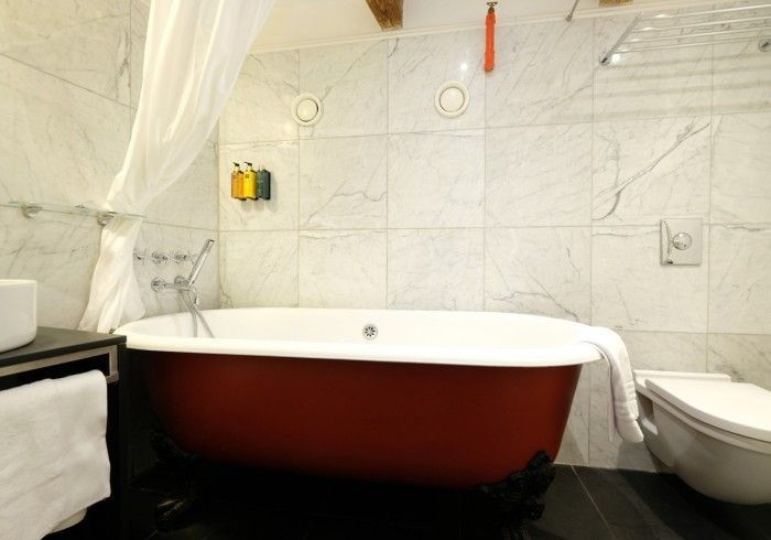 A bathroom with a red bathtub and a toilet