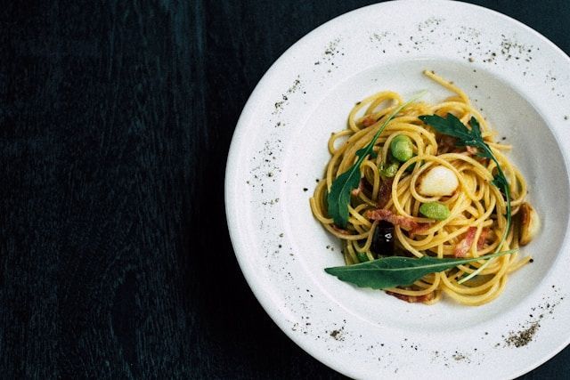 A white plate topped with spaghetti and vegetables on a table.