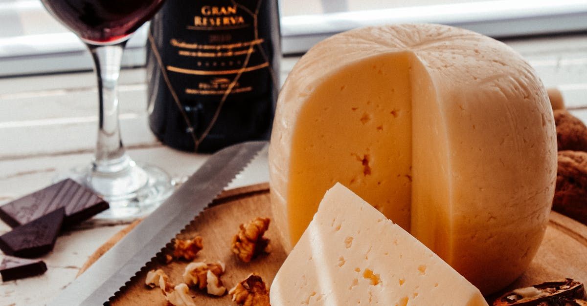 A large piece of cheese is sitting on a wooden cutting board next to a bottle of wine.