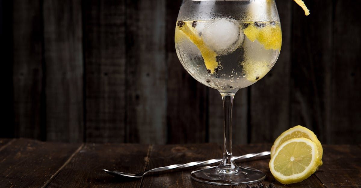 A glass of gin and tonic with ice and lemon slices on a wooden table.