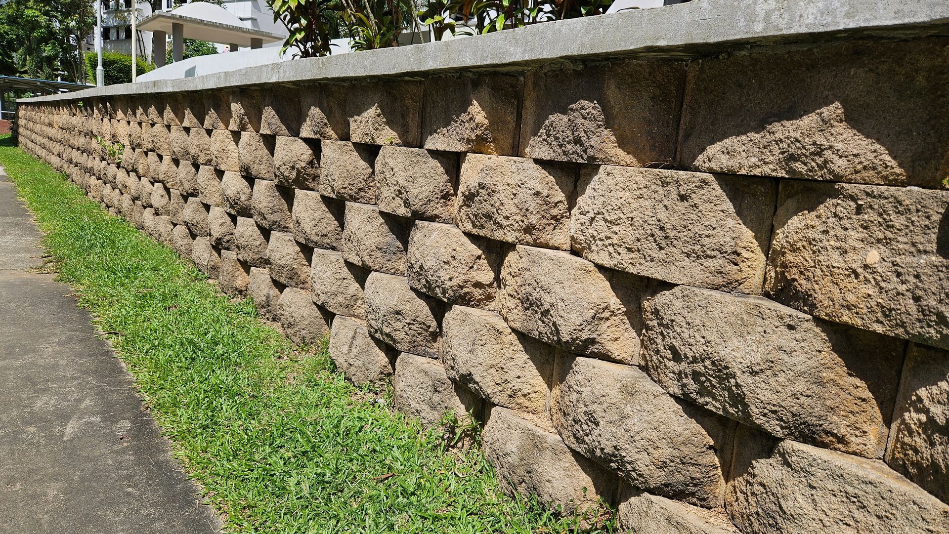 A stone wall is surrounded by grass and a sidewalk.