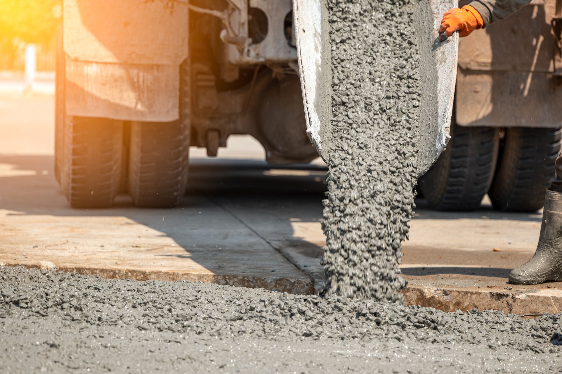 A man is pouring concrete from a truck onto a sidewalk.