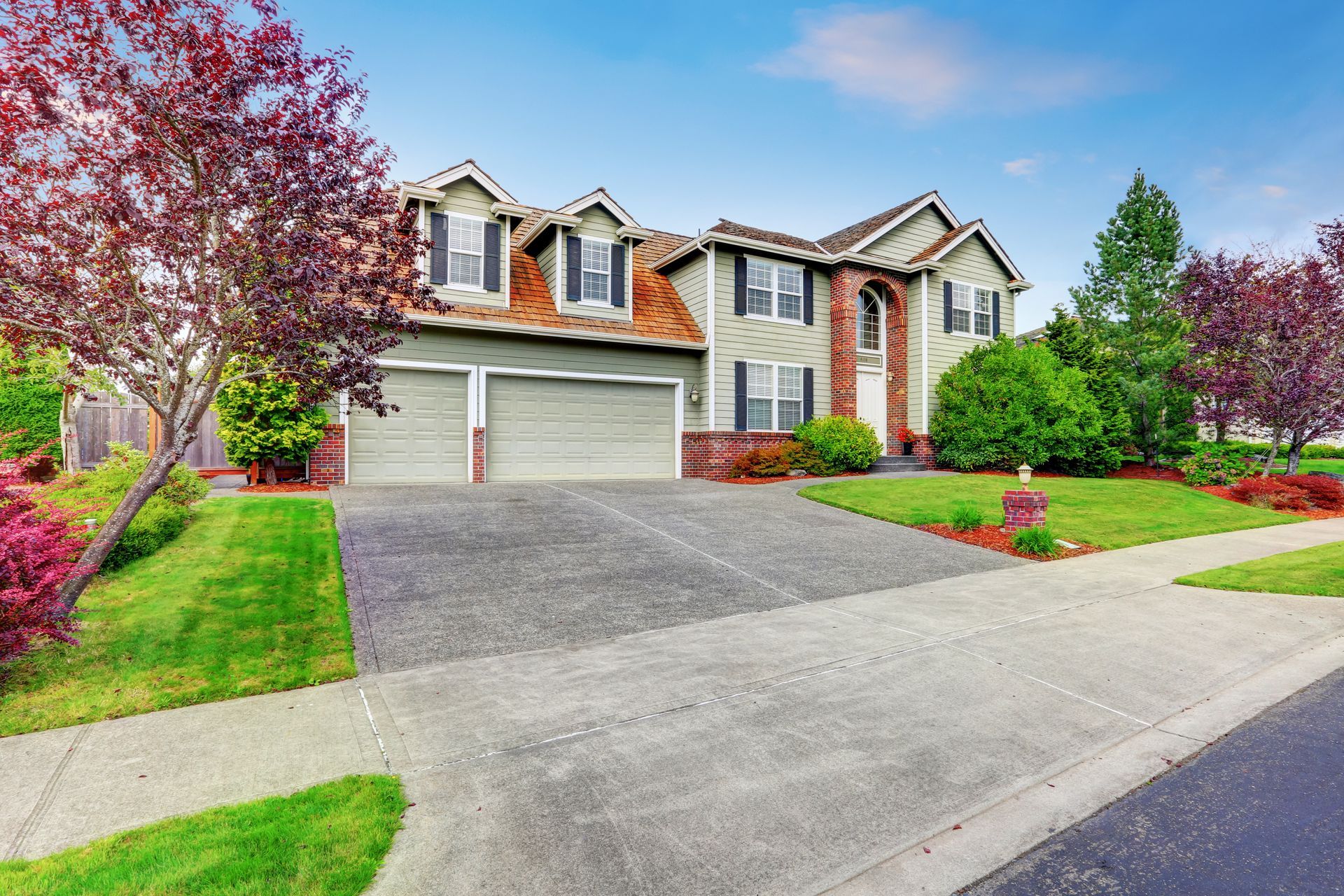 A large house with a large driveway and a lush green lawn.