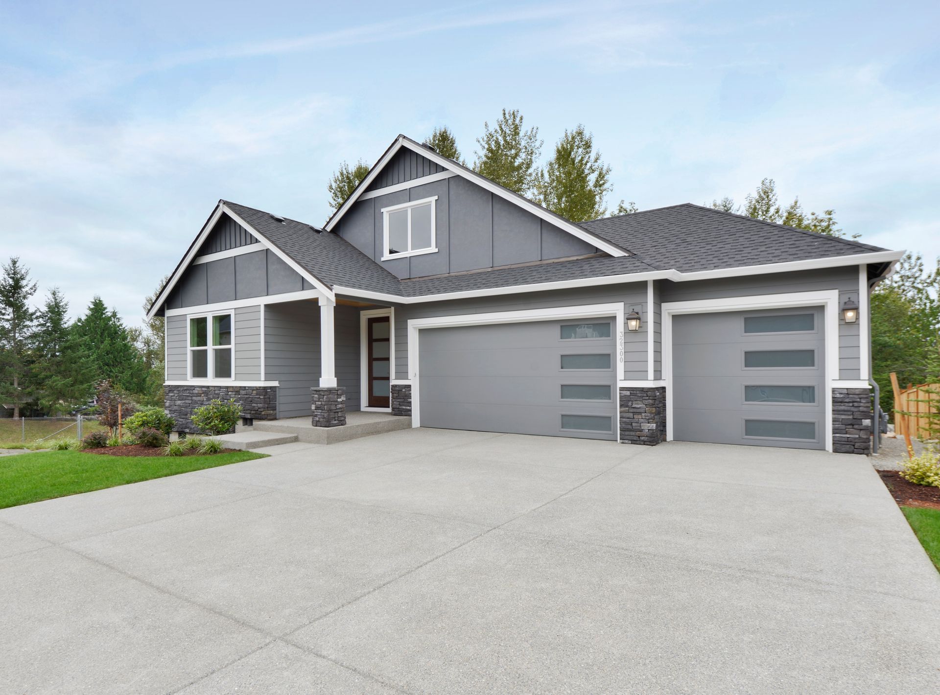A gray house with two garage doors and a concrete driveway