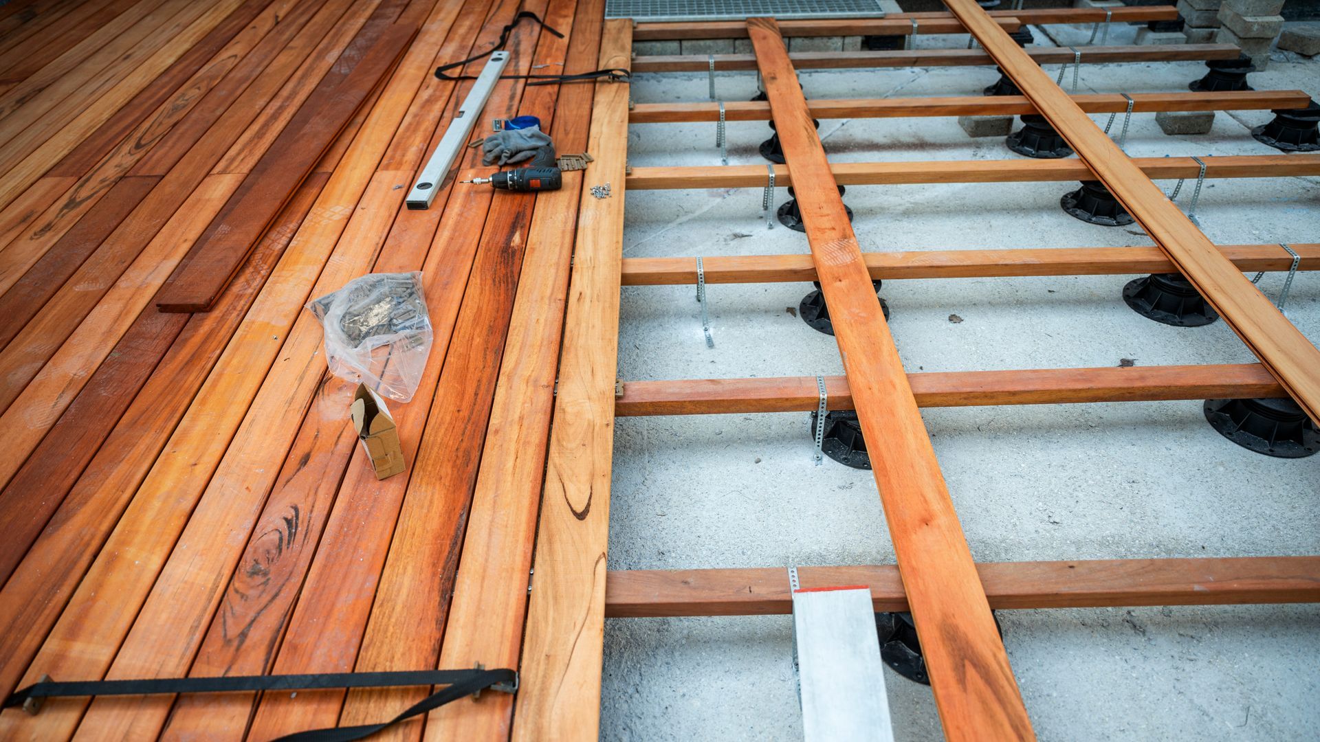 Deck construction: planks being laid over a wooden frame, tools visible, partially complete.