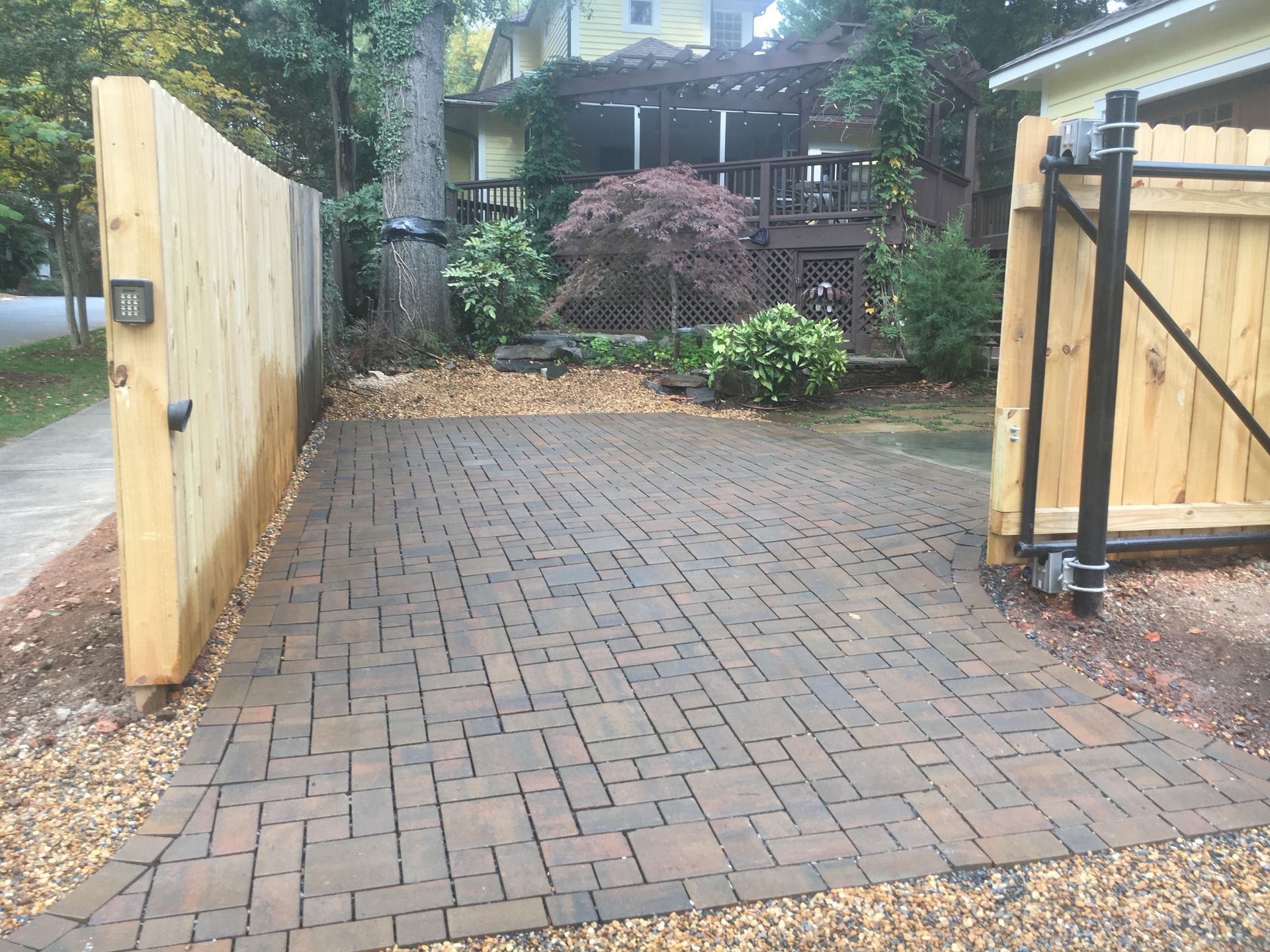 a brick driveway leading to a house with a wooden fence