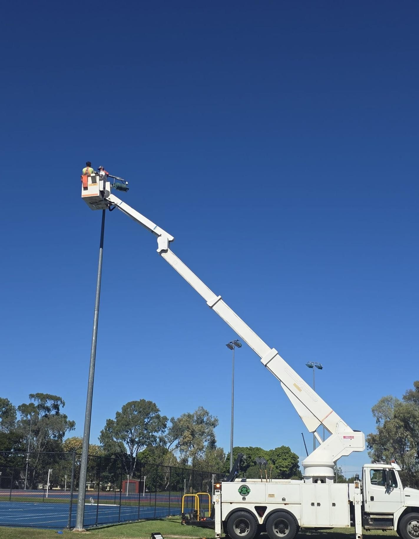 Man On An Aerial Lift Change Out Lights On The Netball Courts — Emerald Tree Services Pty Ltd in Emerald, QLD