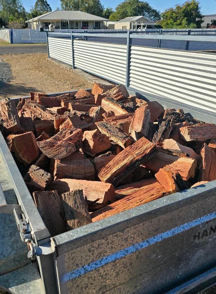 A Pile of Logs is Sitting in a Trailer next to a Fence — Emerald Tree Services Pty Ltd in Emerald, QLD