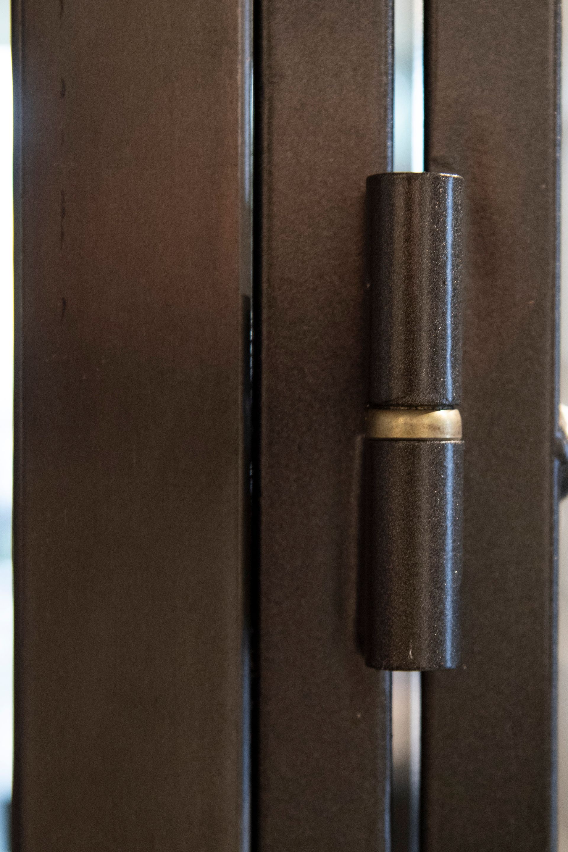 Primo piano di una cerniera per porta color bronzo, che ne mostra la forma cilindrica a botte.