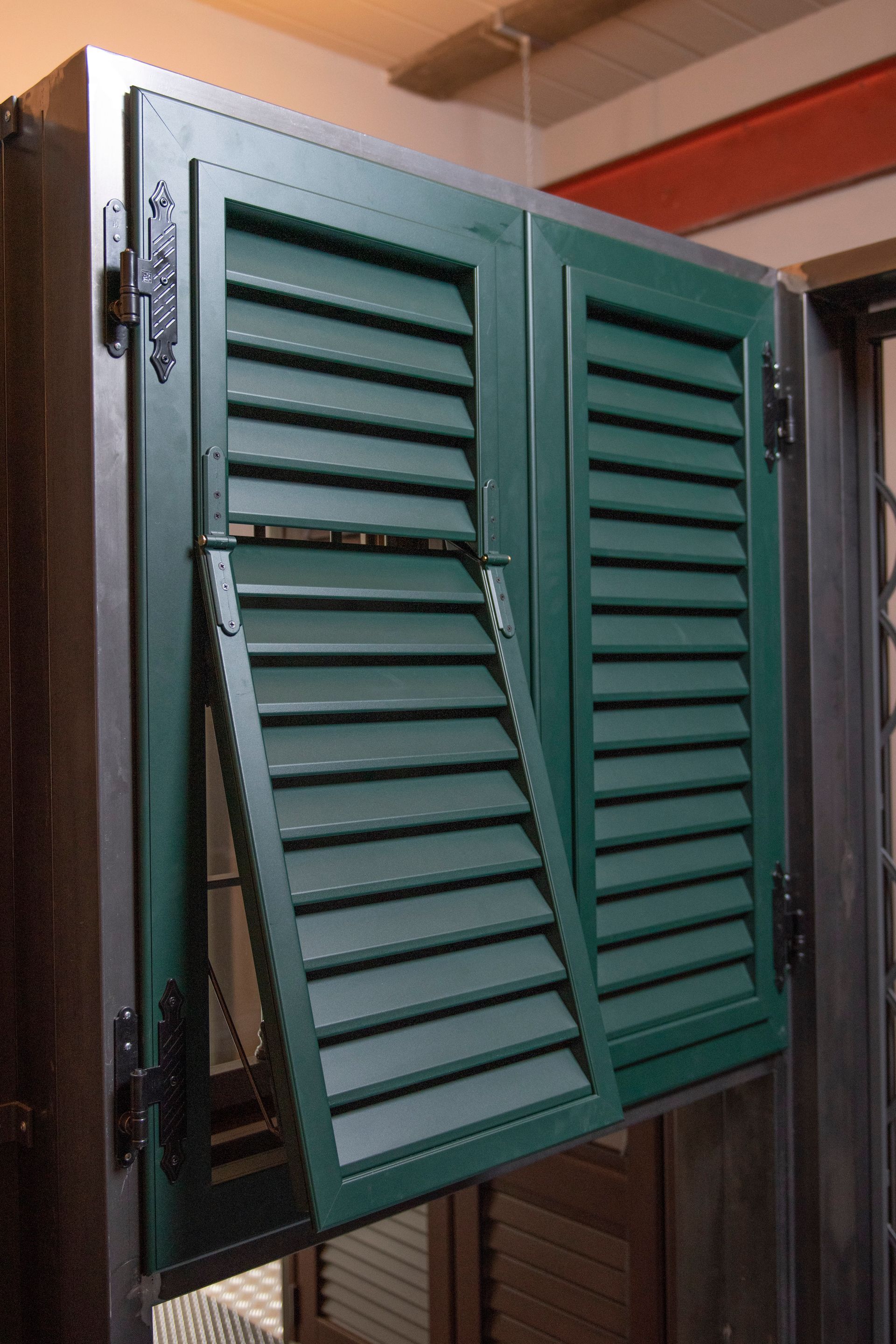 Persiane verdi con persiane, una aperta, montate su un telaio scuro, all'interno.