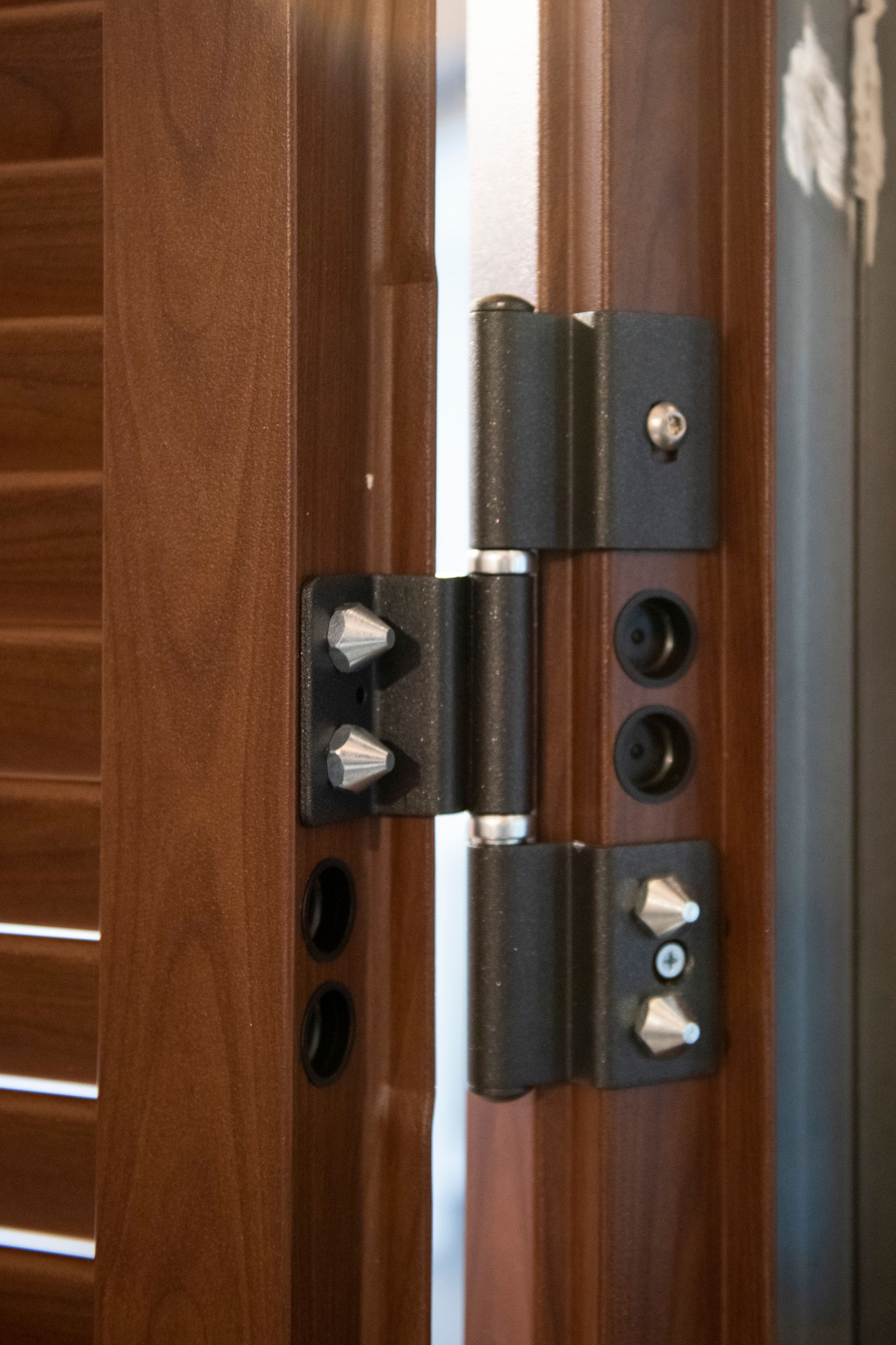 Cardine di un cancello in metallo nero con viti argentate su un cancello in legno marrone.