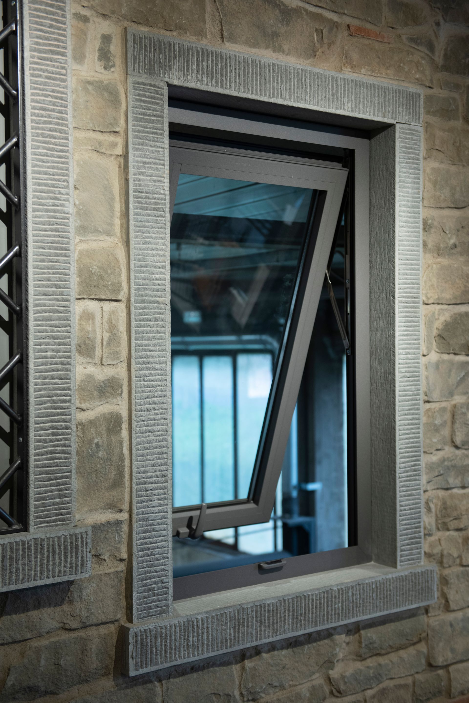 Finestra grigia, aperta ad angolo, incastonata in un muro di pietra.