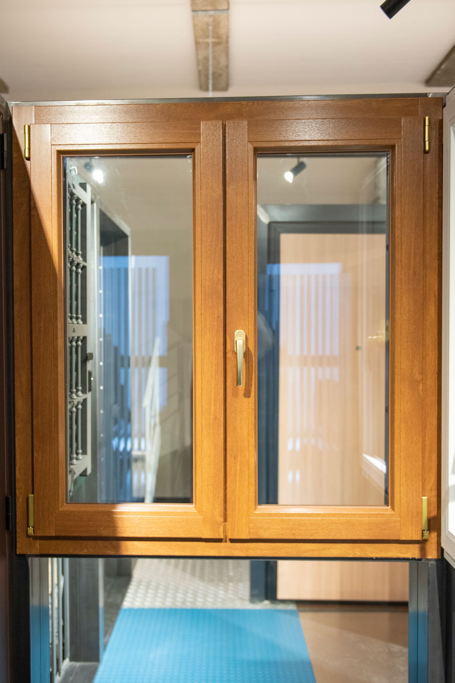 Doppia finestra con telaio in legno e vetri chiusi; vista dall'interno con scorcio di corridoio interno.