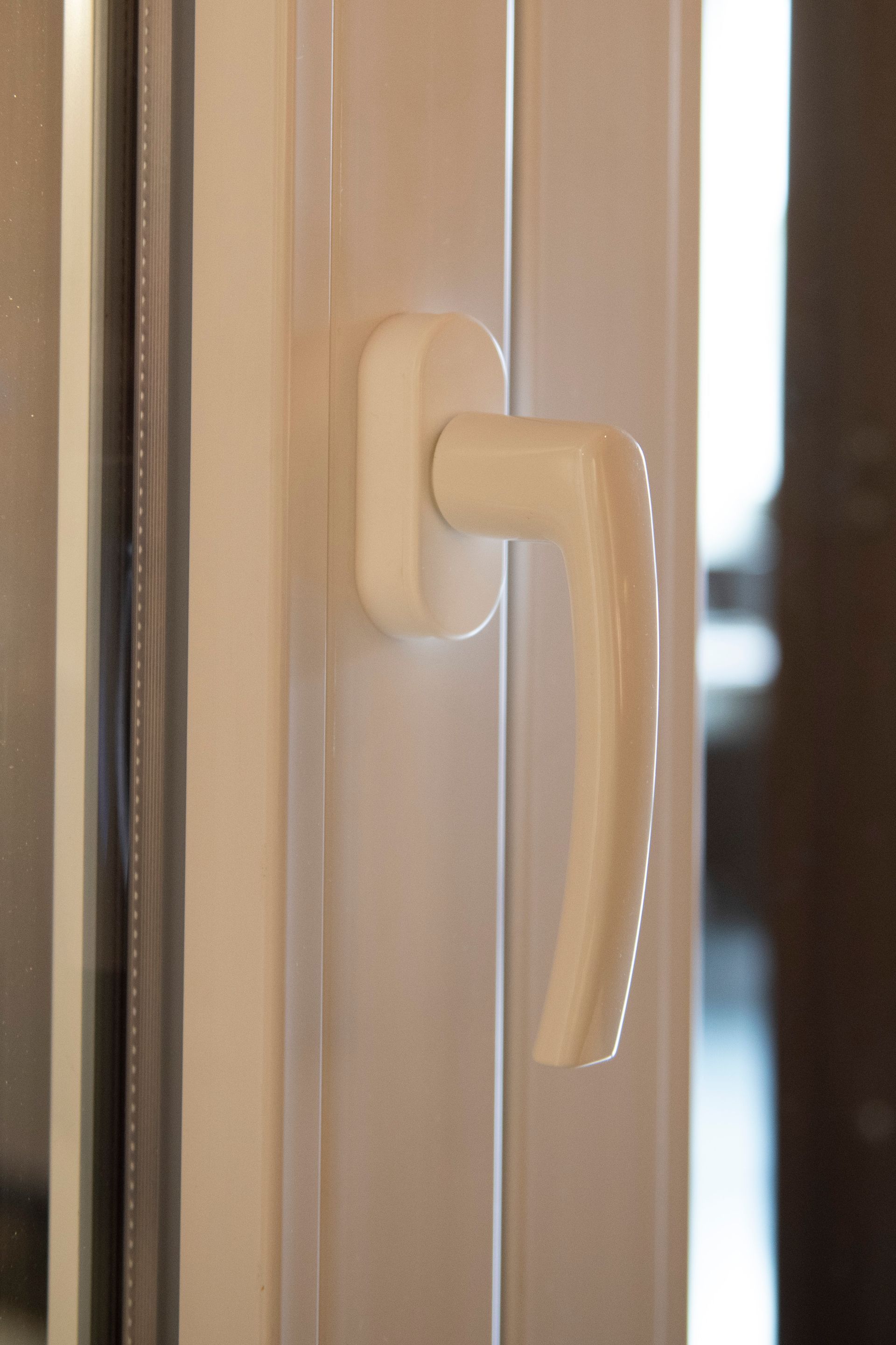 Maniglia bianca per finestra su telaio bianco, parzialmente aperta.