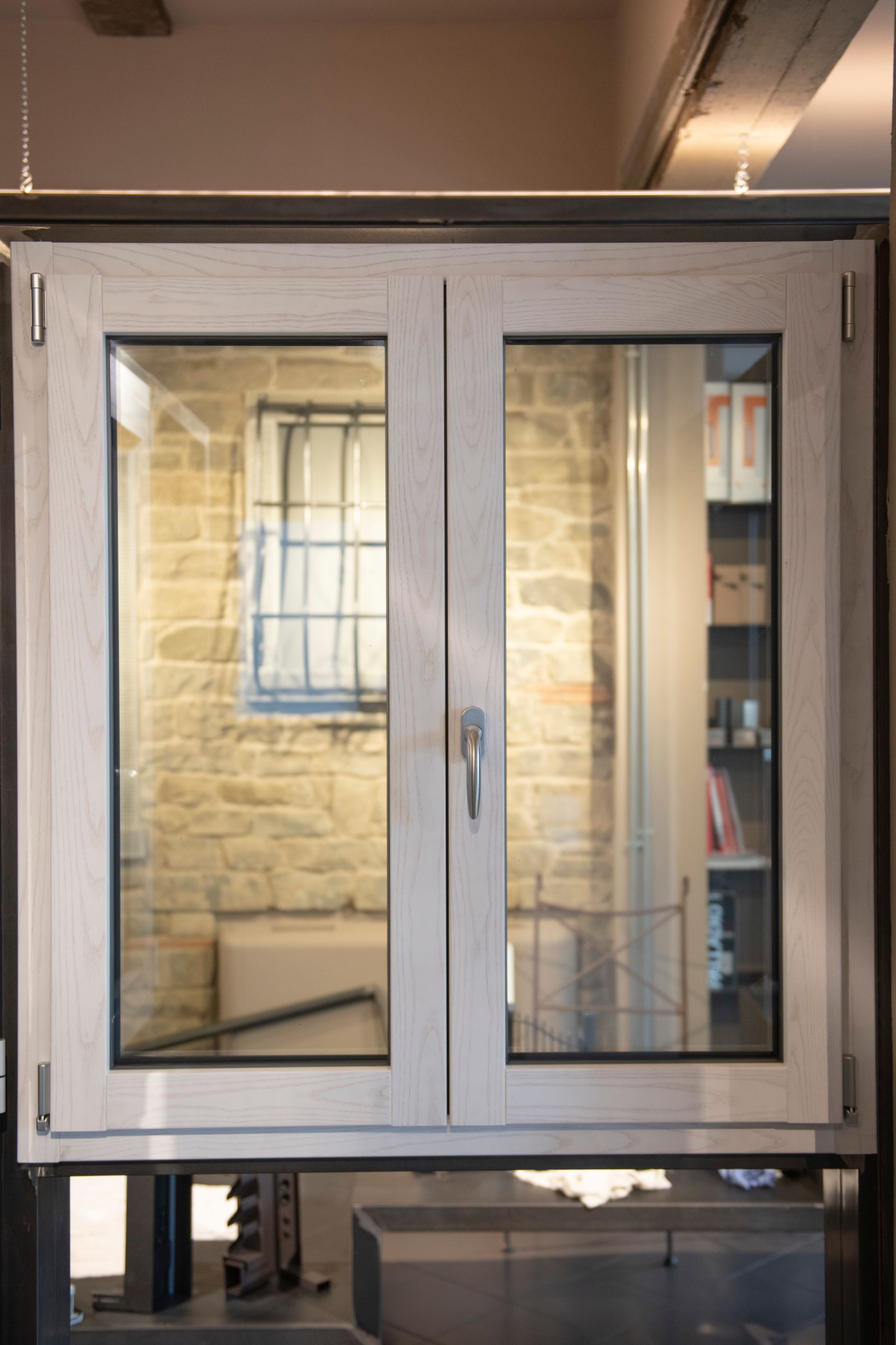 Finestra con doppi vetri e telaio in legno chiaro, che riflette un muro in pietra e interni con mensole.