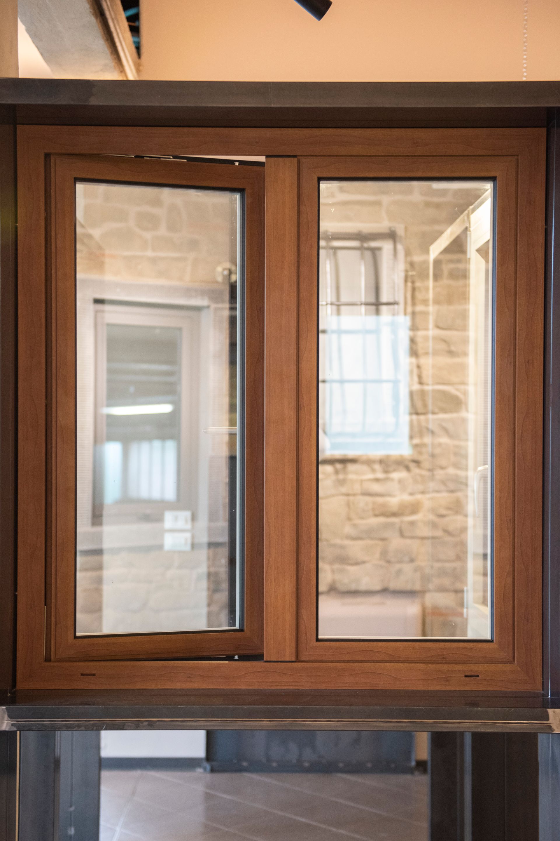 Finestra a doppi vetri con cornice marrone, di cui uno leggermente aperto, che riflette l'interno di un edificio in mattoni e della stanza.