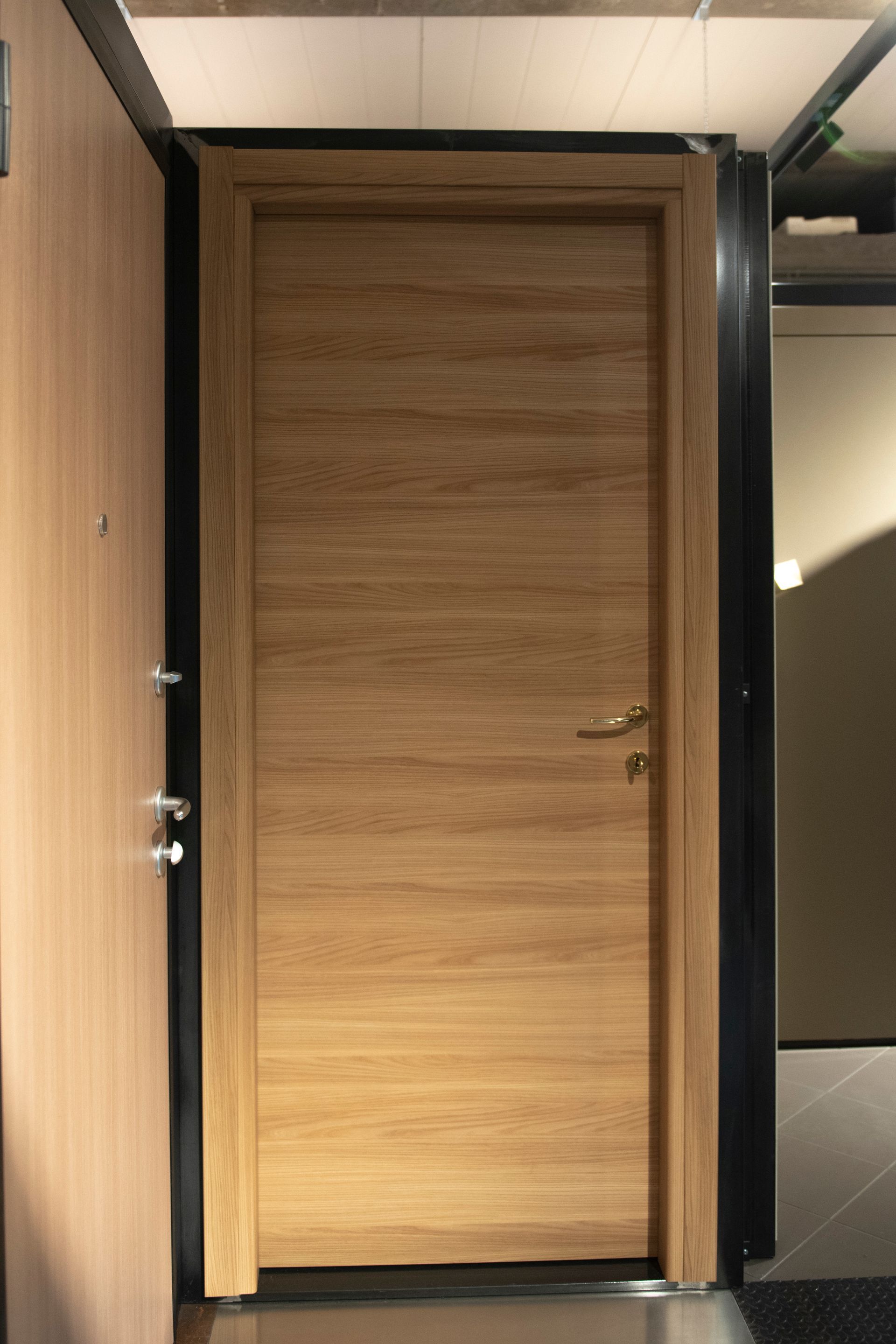 Porta in legno con venature chiare, incorniciata da profili scuri e con maniglia argentata.