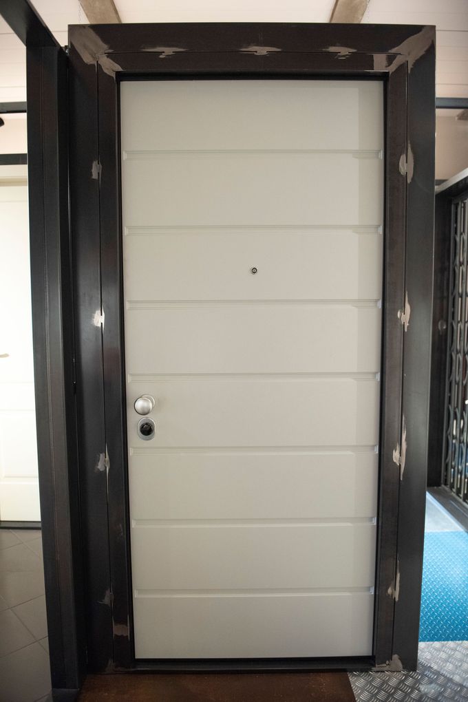 Porta in acciaio grigio con pannelli orizzontali, inserita in una cornice in legno scuro con dettagli metallici decorati.