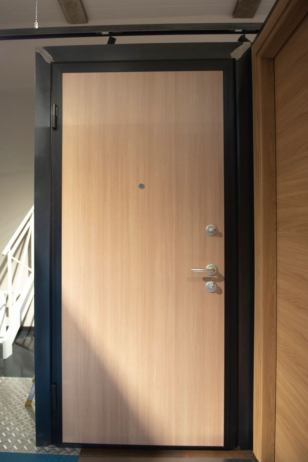 Una porta di legno con finiture nere, maniglia e spioncino; ambientazione del corridoio.