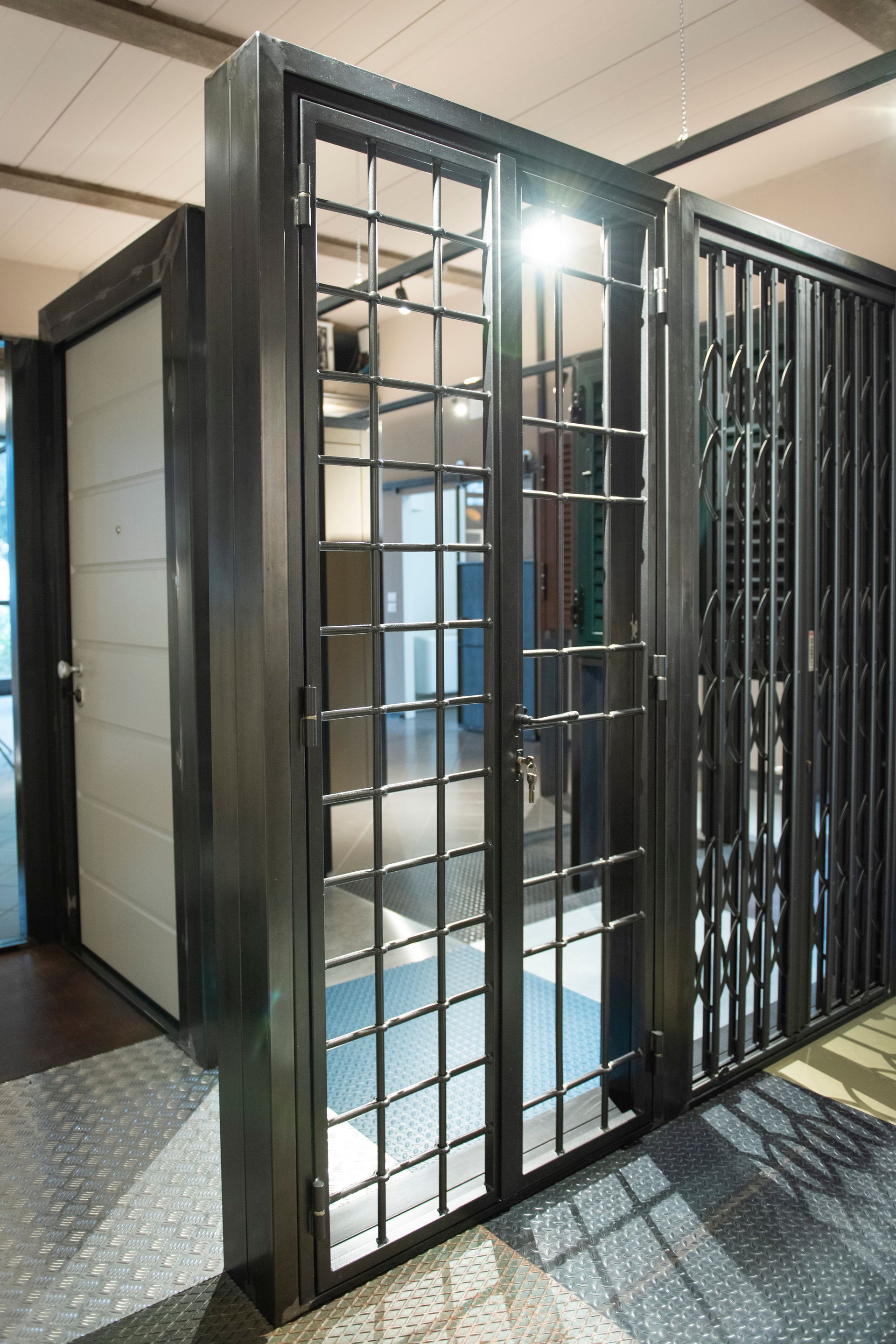 Cancelli di sicurezza in metallo con sbarre verticali e orizzontali conducono a un corridoio con una porta bianca.
