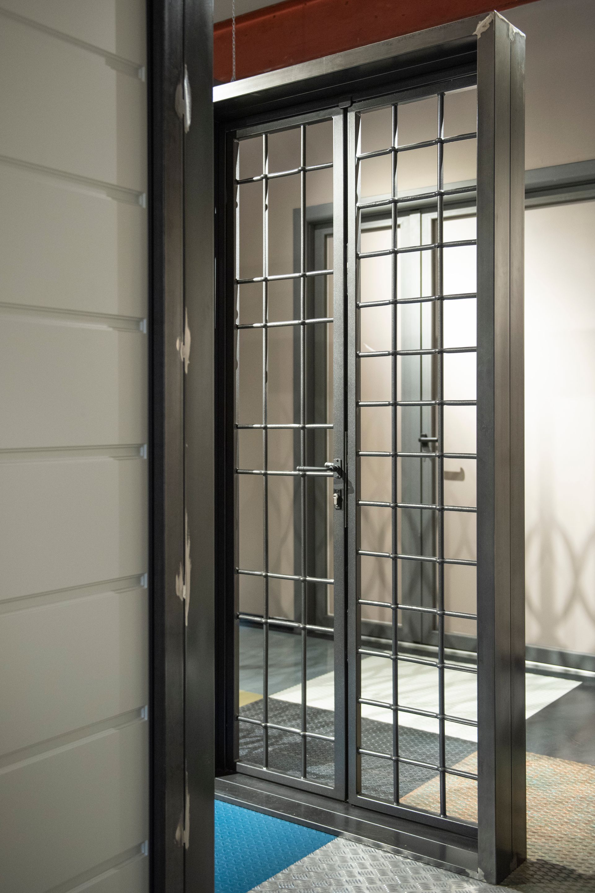 Porta di sicurezza aperta in metallo con sbarre verticali e orizzontali.