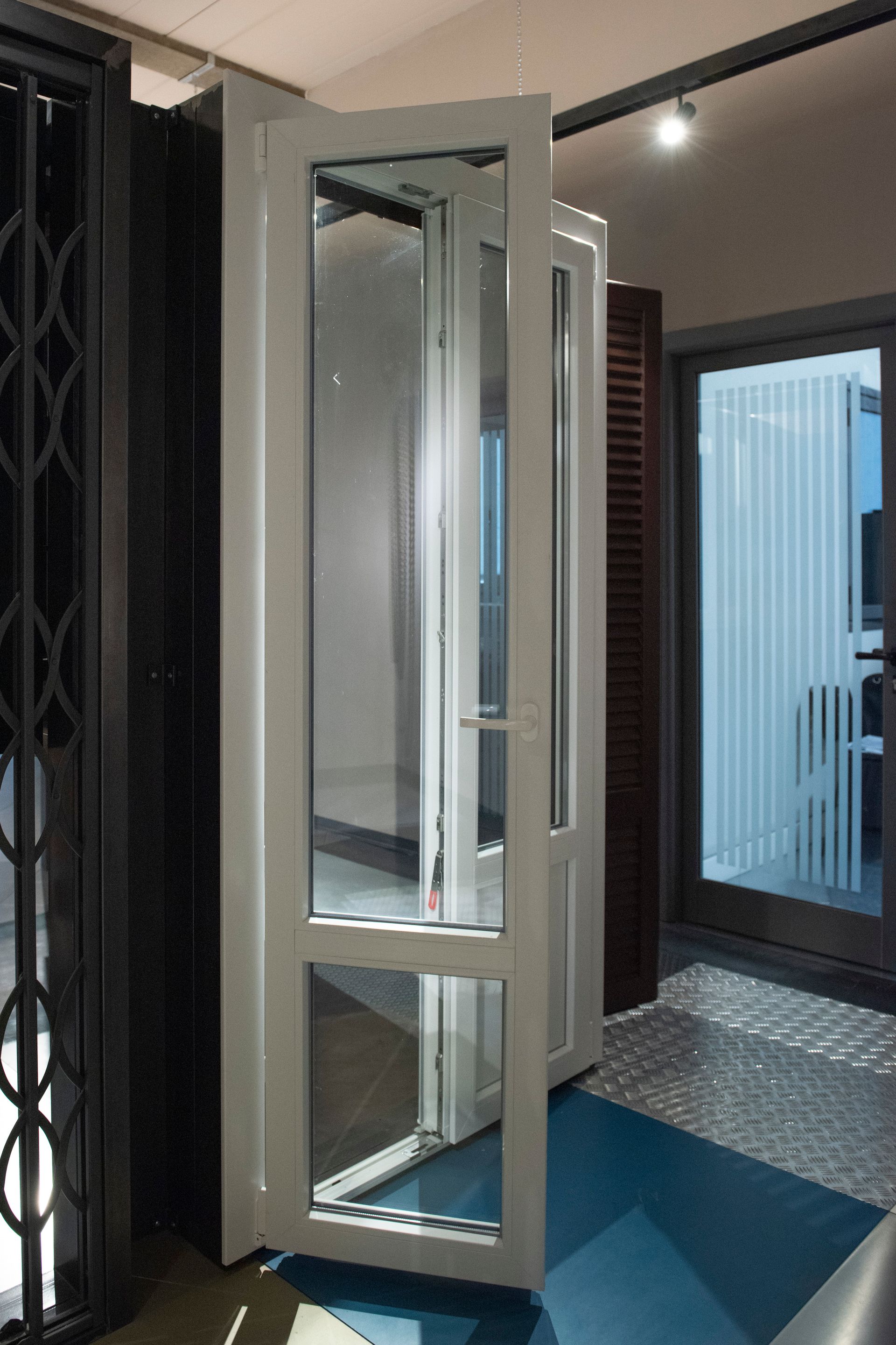 Porta in vetro bianco, parzialmente aperta, per interni. Esposizione di vari stili di porte, ambientazione showroom.