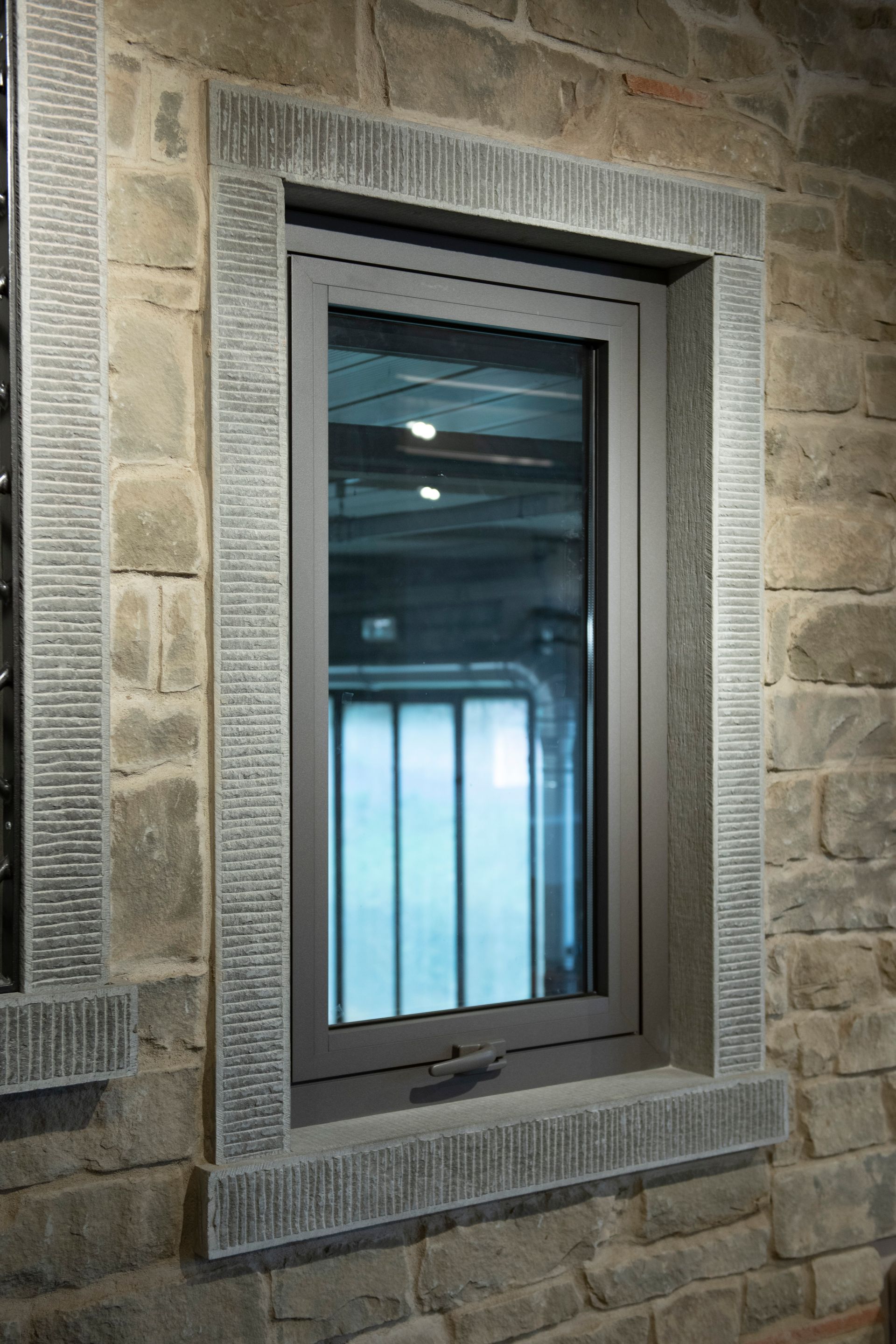 Finestra grigia in un muro di pietra, incorniciata da pietra grigia testurizzata.