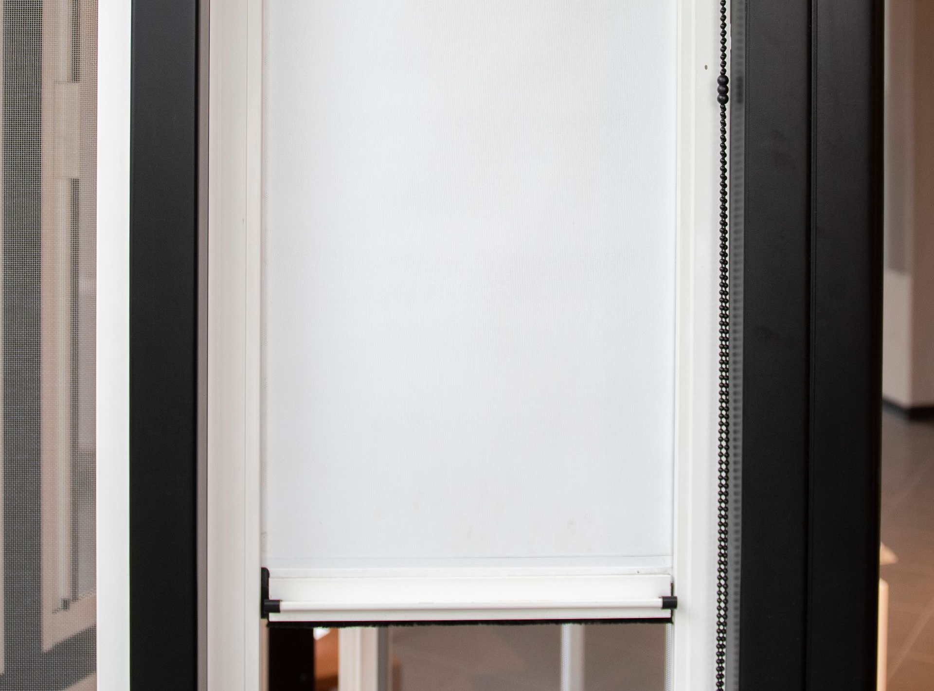 Tenda a rullo bianca parzialmente abbassata nel telaio nero della finestra.
