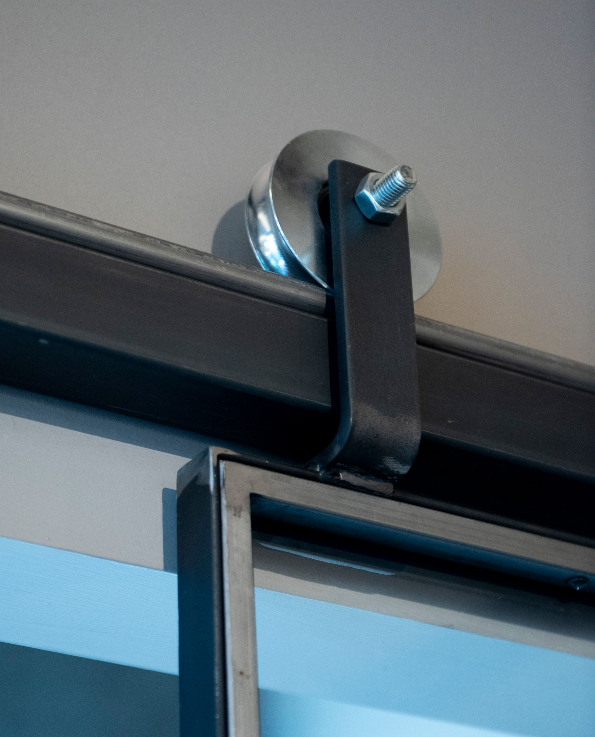 Ferramenta per porte da fienile: binario in metallo nero con rullo fissato al telaio della porta, montato sul soffitto.